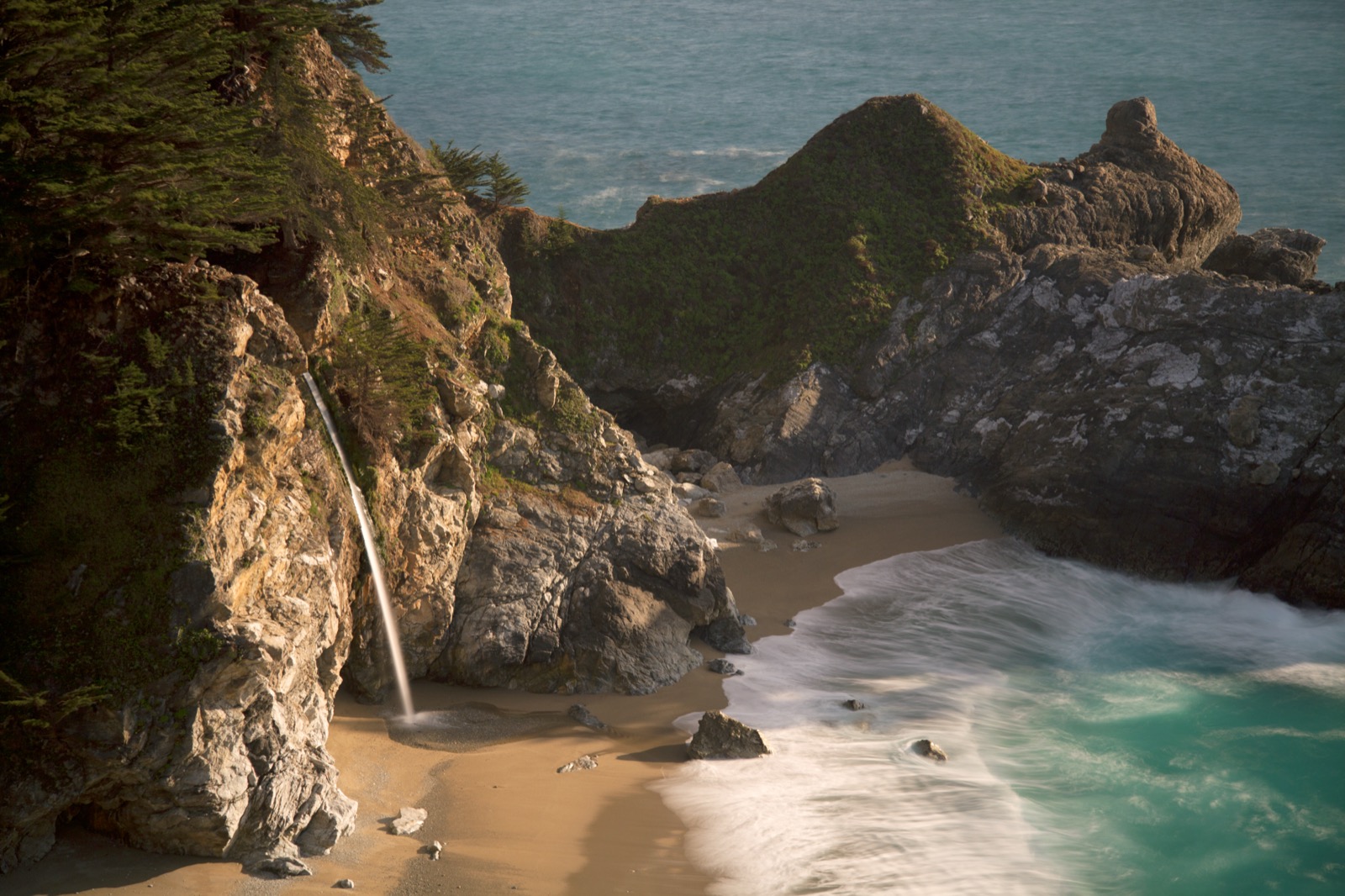 Waterfall cascading onto a secluded Big Sur cove at golden hour
